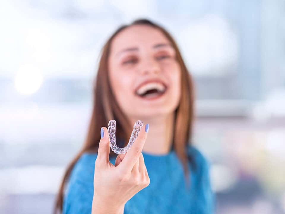 woman is laughing and smiling as she holds her new clear braces
