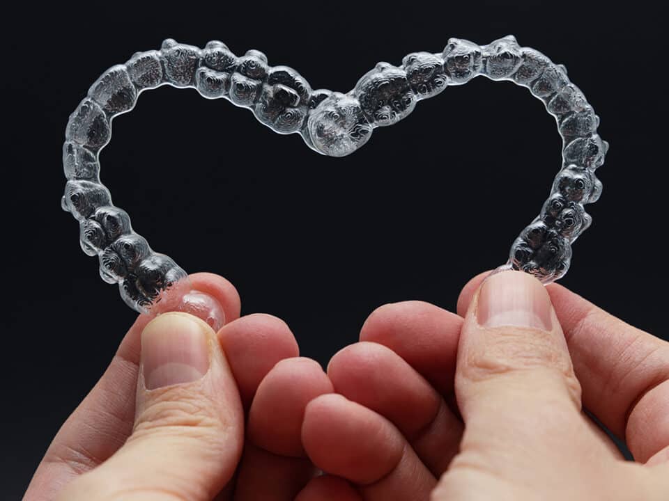 man holds two clear aligner trays together to form the shape of a heart