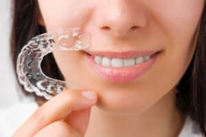 woman smiles and holds her new clear braces in her hand