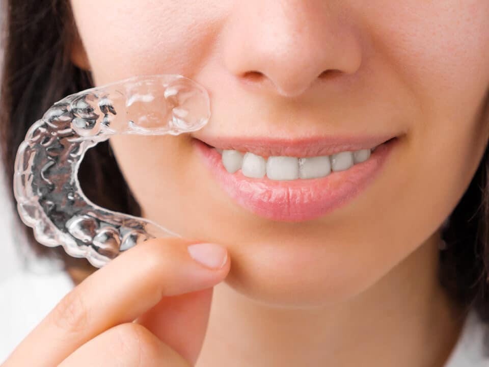 woman smiles and holds her new clear braces in her hand