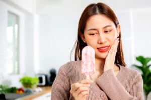 woman holds the ice cream bar that has caused her tooth sensitivity to flare up