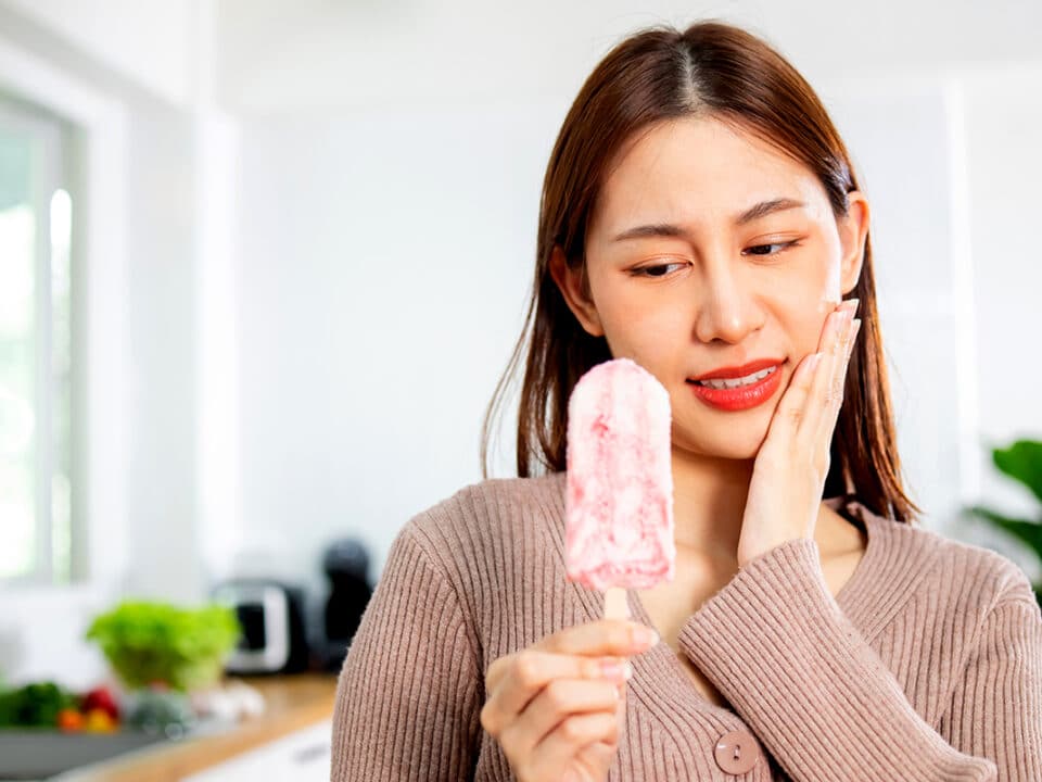 woman holds the ice cream bar that has caused her tooth sensitivity to flare up