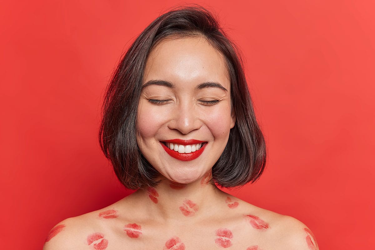 woman on a red background smiling and showing off her very feminine smile