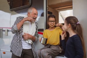 grandpa and granddaughters brush their teeth outside an RV while on vacation