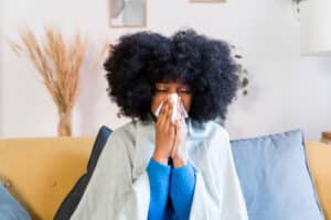 woman with a big fro blows her nose while sitting on a couch