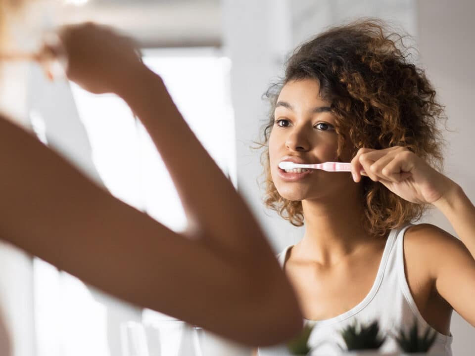 young woman stands in front of the mirror brushing her teeth properly