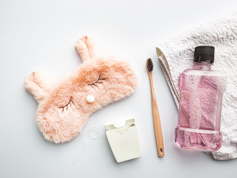 a bunny shaped sleep mask, some floss, a toothbrush and some mouthwash lie on a towel