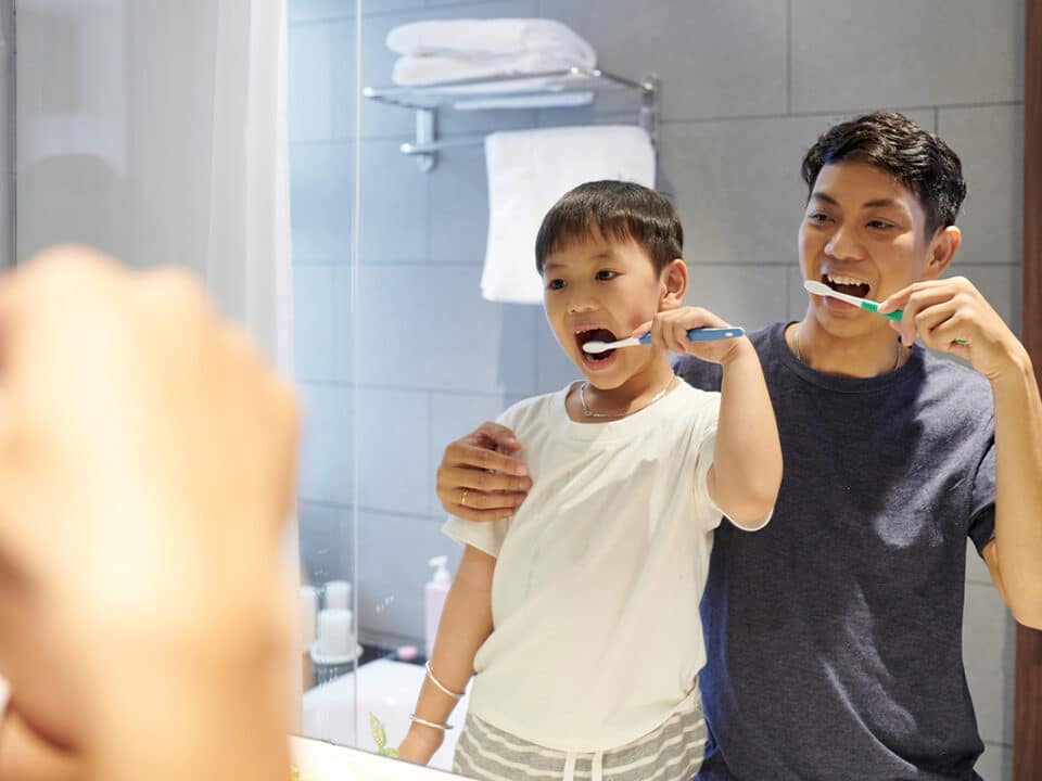father and son brush their teeth together in the mirror