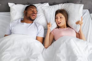 woman holds a pillow against her head to try and drown out the noise of her partner snoring