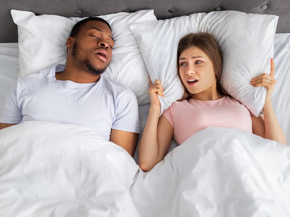 woman holds a pillow against her head to try and drown out the noise of her partner snoring