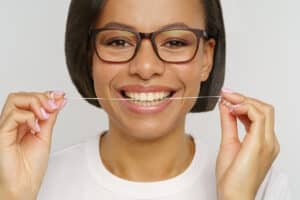 woman with glasses holds a string of floss which is included in the five key steps to good oral health