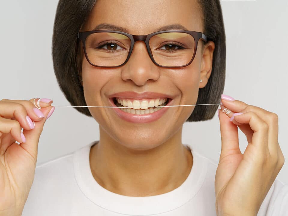 woman with glasses holds a string of floss which is included in the five key steps to good oral health