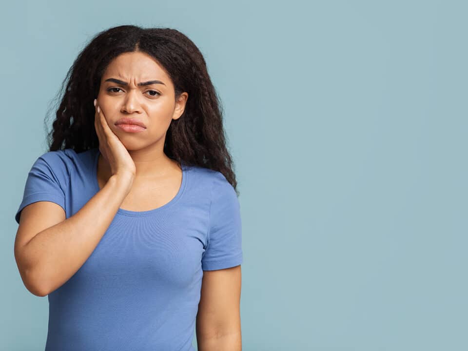 woman in a blue shirt holds her face as she experiences one of the painful symptoms of an abscessed tooth