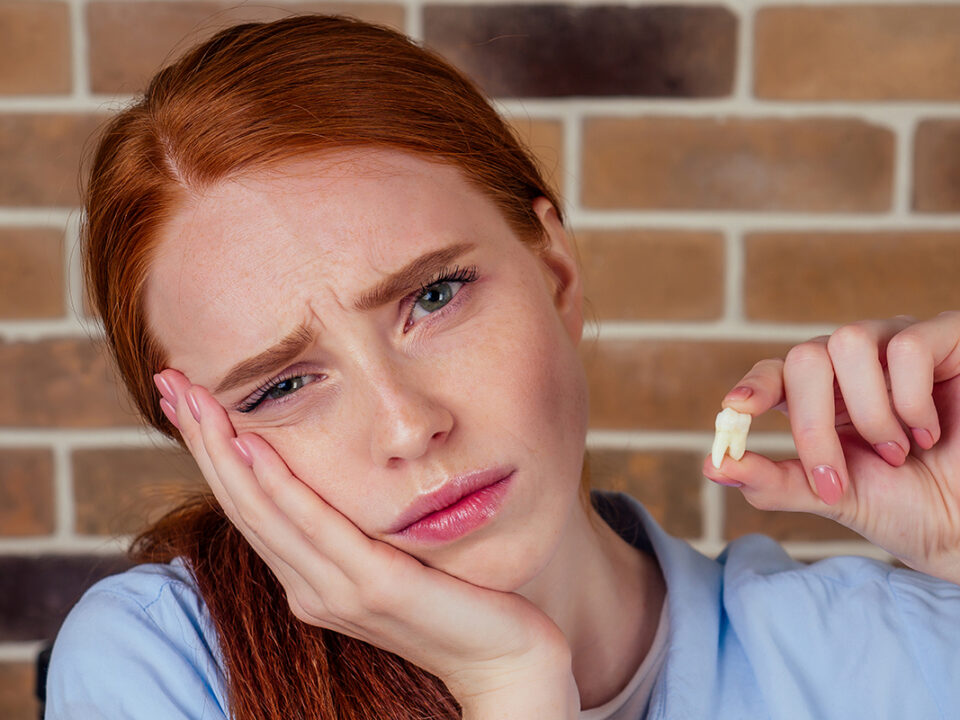 red haired woman looks upset as she holds a tooth as she needs tips to fend of periodontal disease