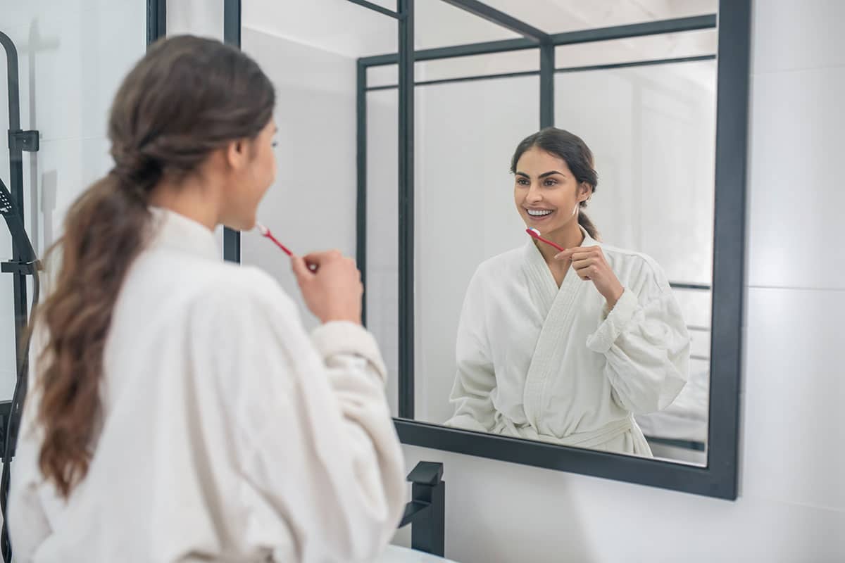 the benefits of a cosmetic dentist are apparent to this woman as she admires her shiny white teeth in the mirror