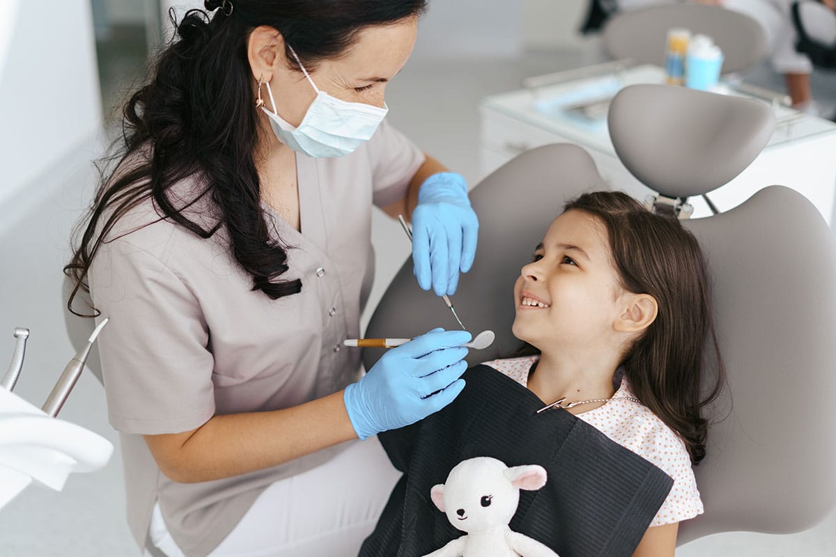small girl with stuffed animal smiling in the dentists chair after her mother learned how to speak to your kids about the dentist