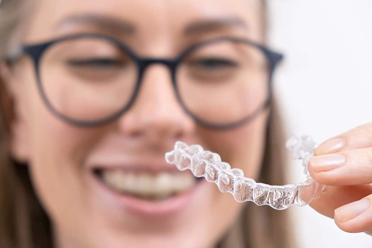 woman in glasses smiling while inspecting an invisalign clear aligner tray 