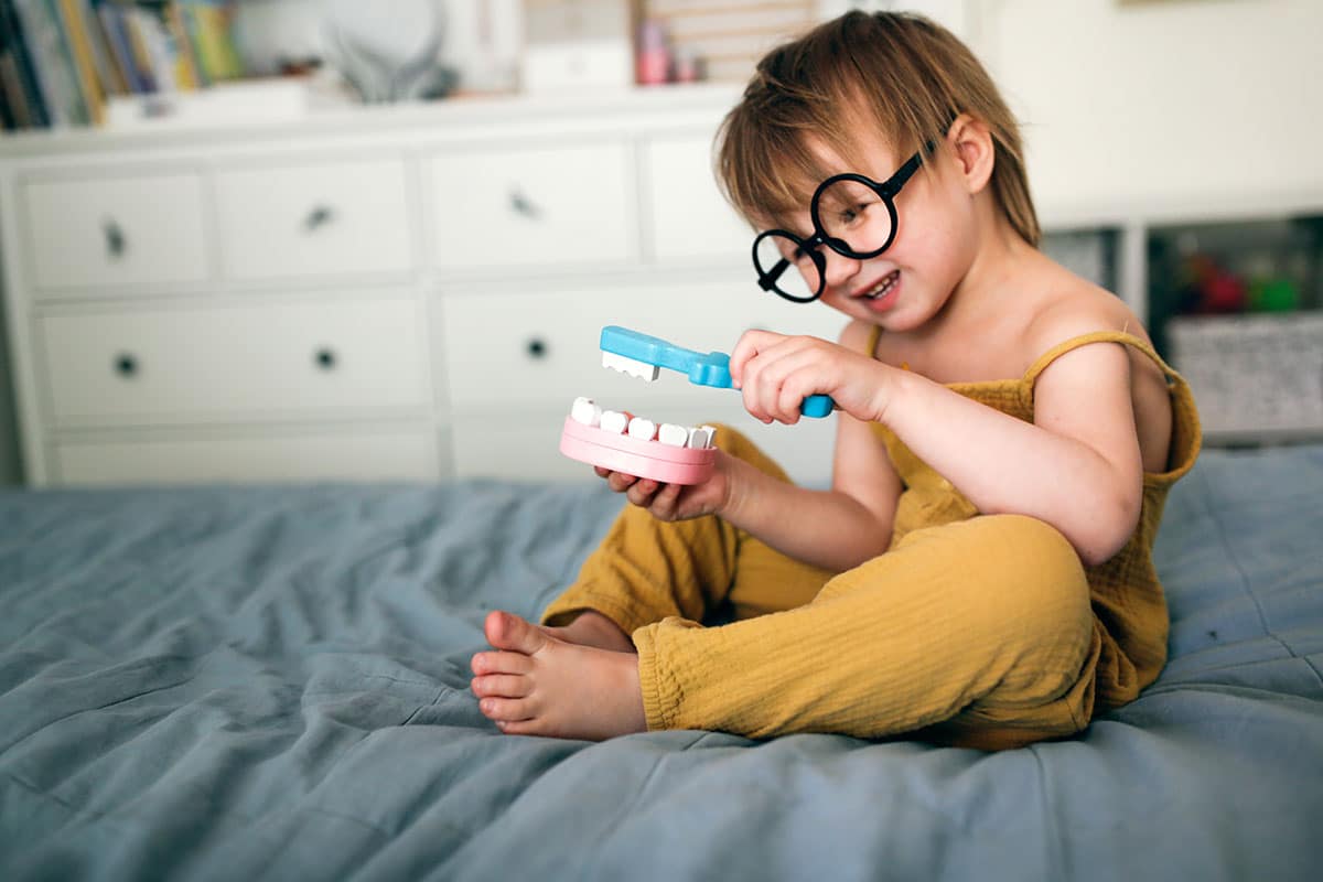 small boy in glasses and yellow pajamas is playing with a set of dentures and a toothbrush