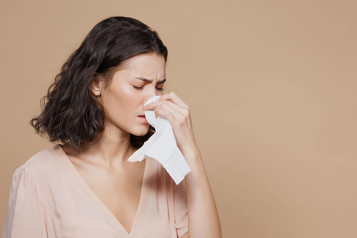 woman blows her nose as she wonders  does a cold or flu affect oral health?