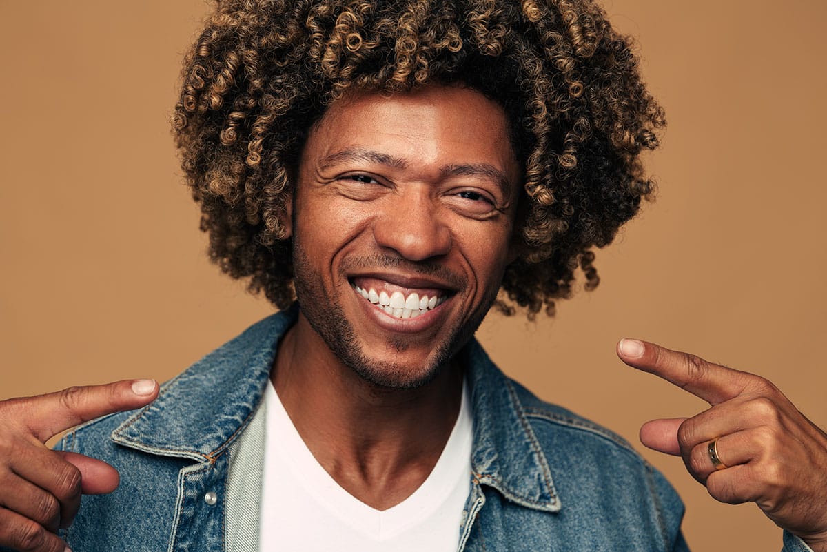 black man points at his amazing smile because he took our advice if you're thinking about dental veneers