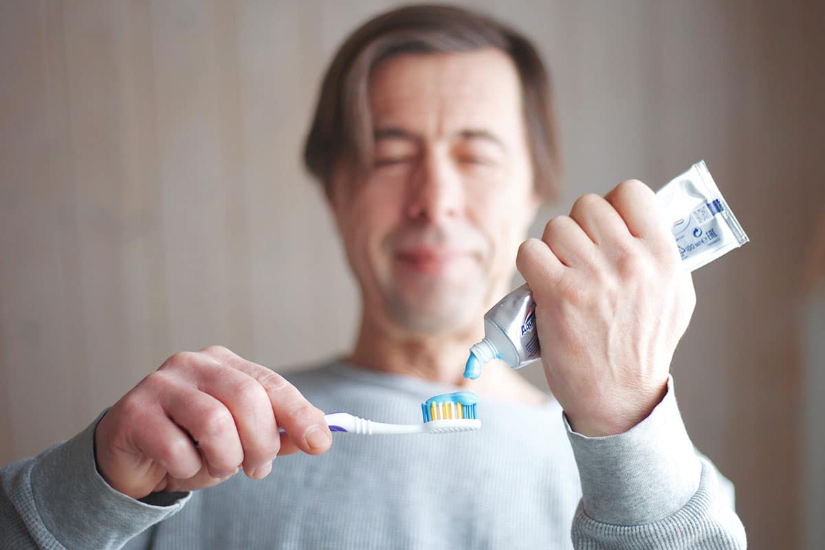 man puts sensitivity toothpaste onto his toothbrush after getting dental veneers