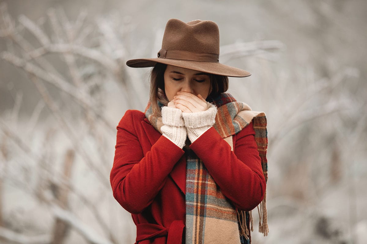woman wearing a stupid hat blows on her hands and wonders if her good oral hygiene is a seasonal flu fighter