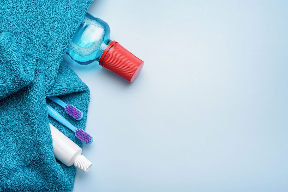 a bottle of mouthwash tucked into a towel alongside toothpaste and toothbrushes as part of the 8 useful benefits of using mouthwash