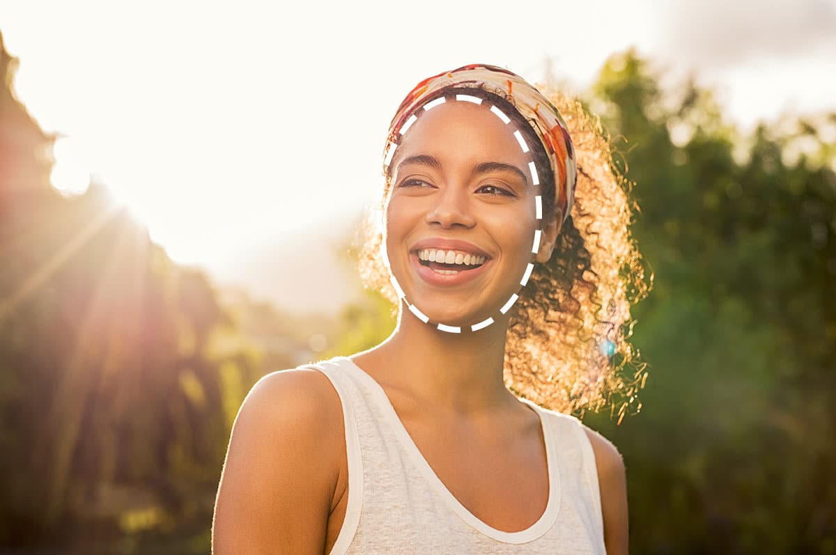 woman with an oval shaped face smiling with the sun behind her