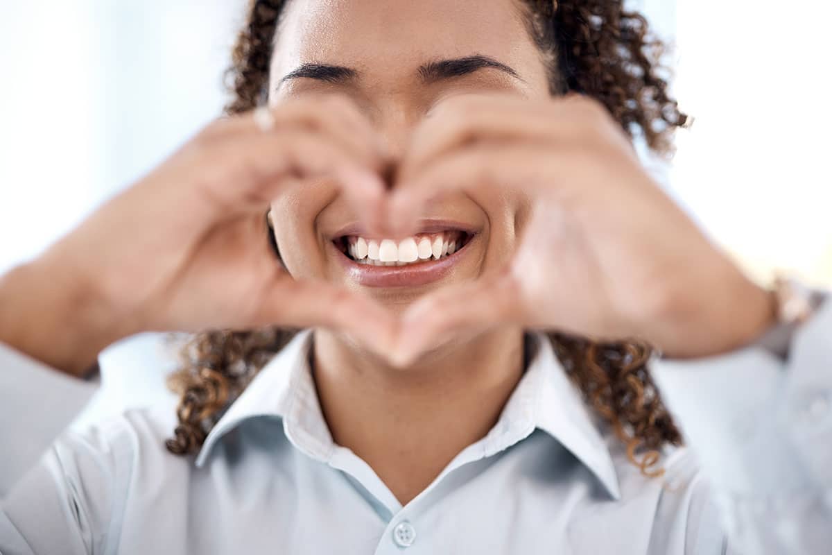 women making the heart sign with her hands while answering the question of what shape of teeth are best for my face