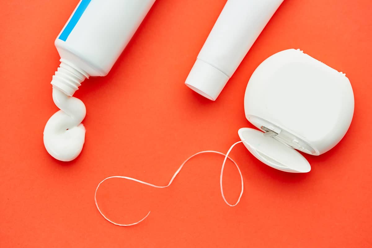 a photo of some toothpaste and a roll of dental floss on an orange background