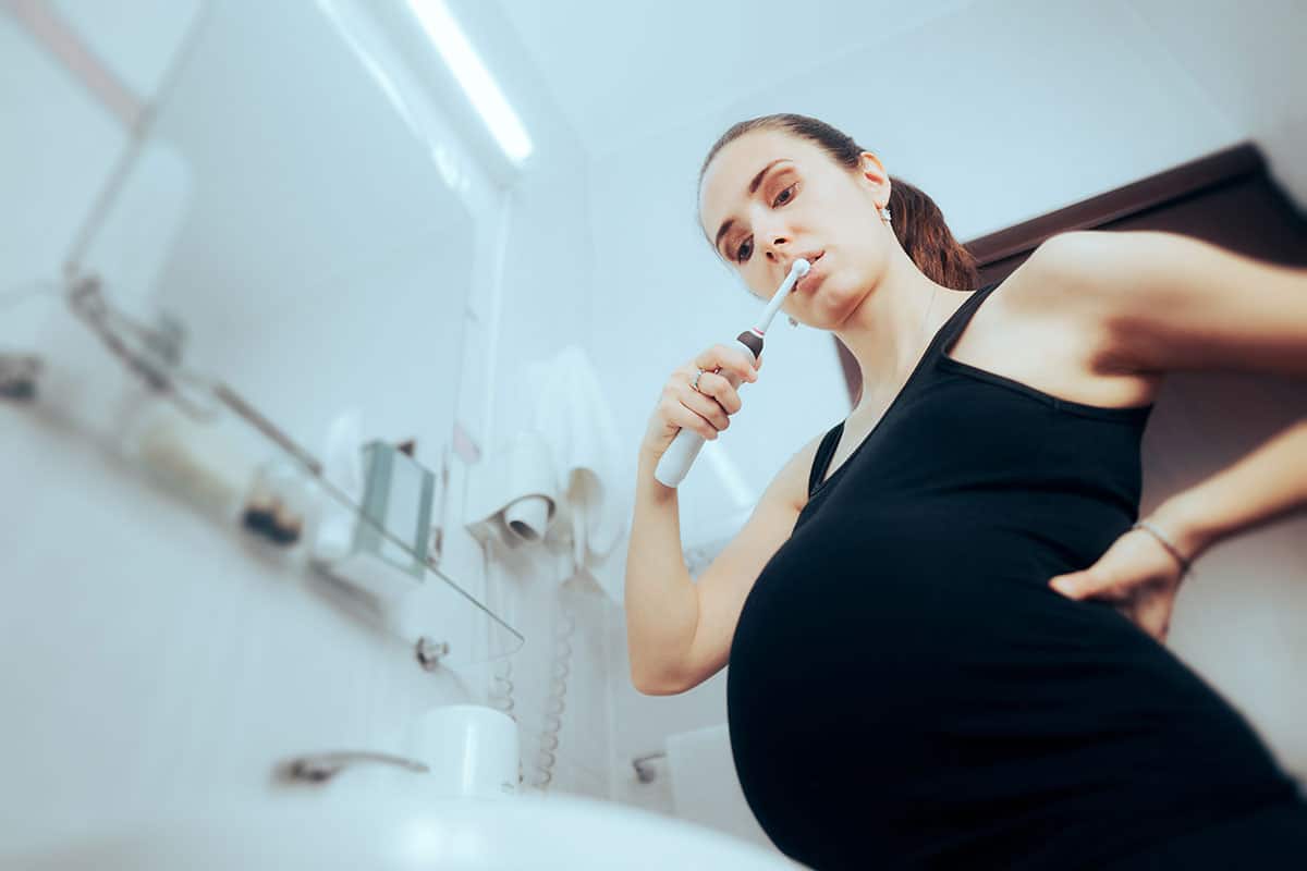 pregnant woman is brushing her teeth in the bathroom wondering is going to the dentist while pregnant dangerous