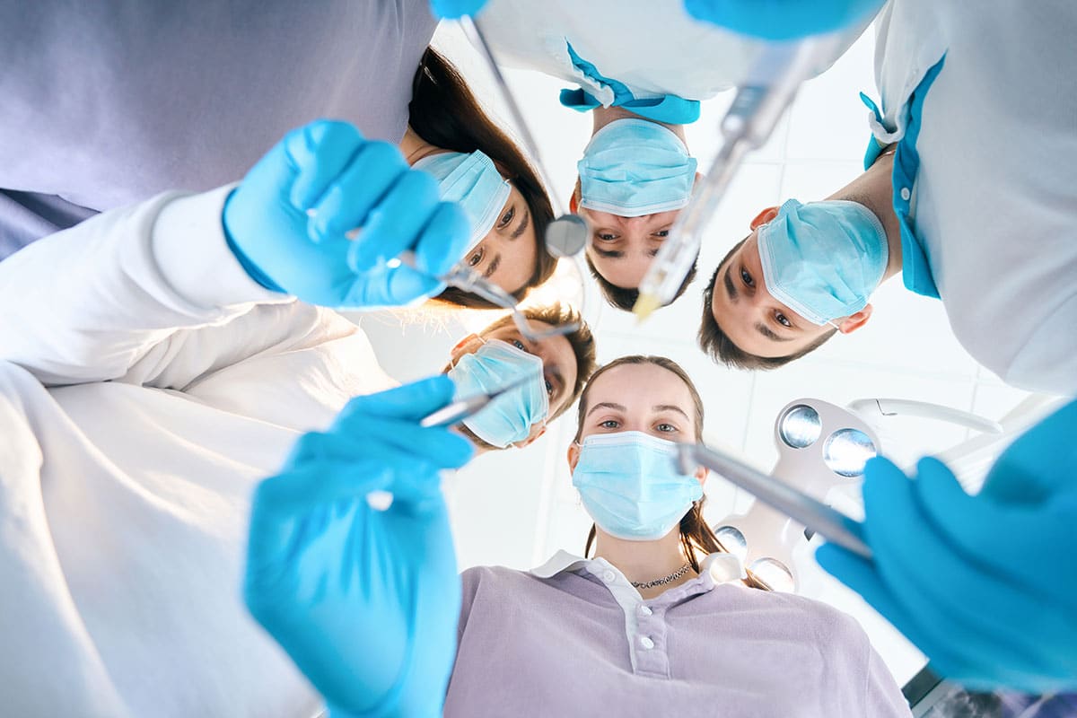 pov of a patient in the dentist chair as oral surgeons lean in with tools in hand