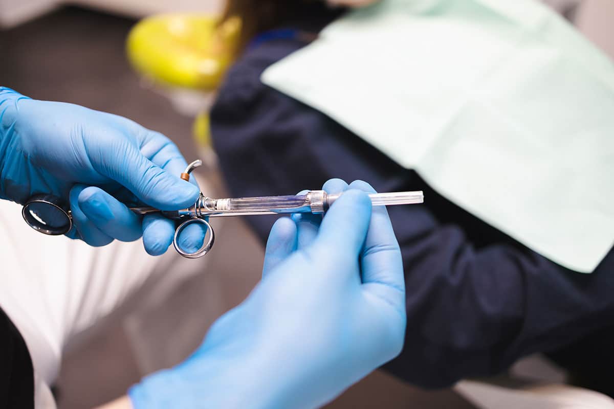 dentist with blue latex gloves on holds a needle full of dental anethetic