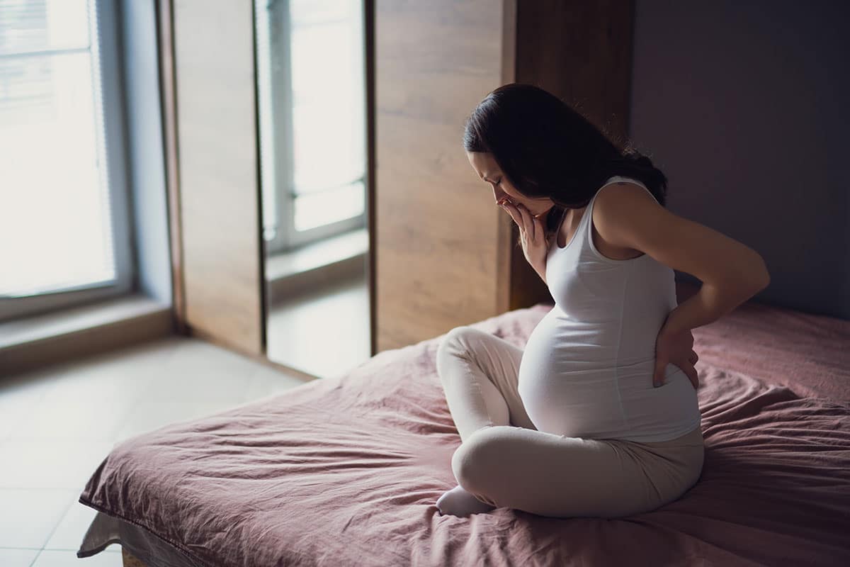 pregnant woman sits on a bed in pain from periodontal disease as she wonders is gum disease can affect pregnancy outcomes