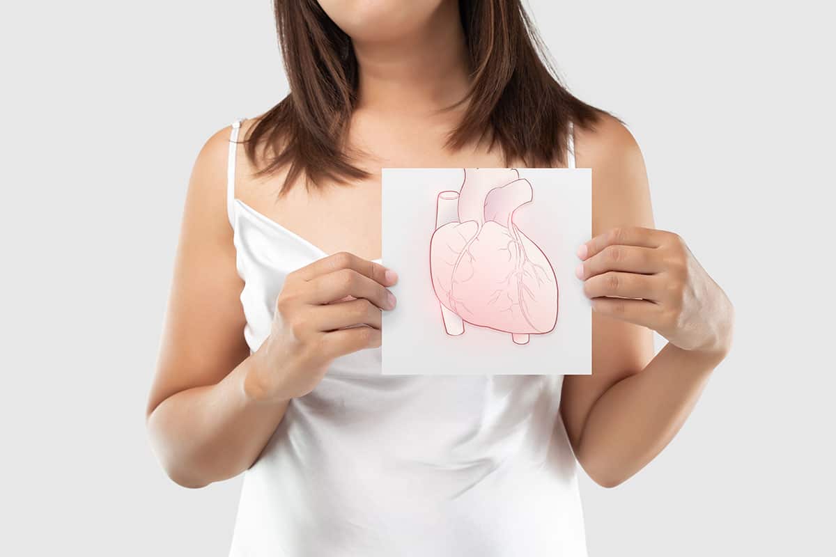 woman holds a hand drawn picture of a human heart in front of her chest to portray the link between gum disease and heart disease