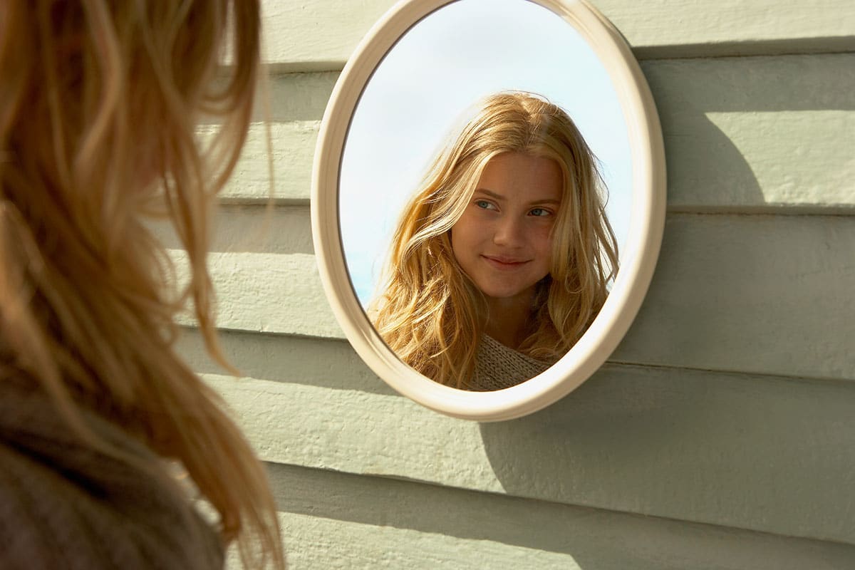 young blonde girl practicing smiling in the mirror