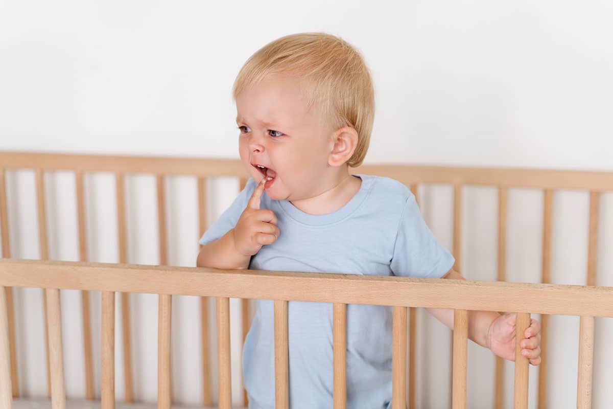 baby standing up in his crib crying because teething is painful