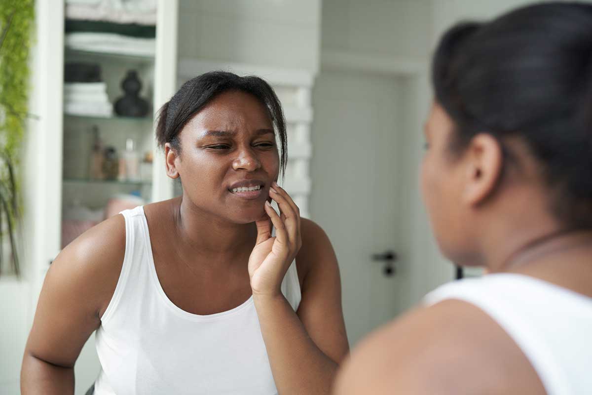 woman looking in the bathroom mirror and holding her jaw because of the bruxism pain