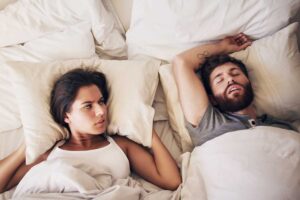 couple in bed and the woman is looking at her man angrily because he's snoring due to his untreated sleep apnea