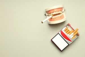 image of dentures with a cigarette dangling between the teeth as the featured image for our article on how to keep teeth white even if you smoke