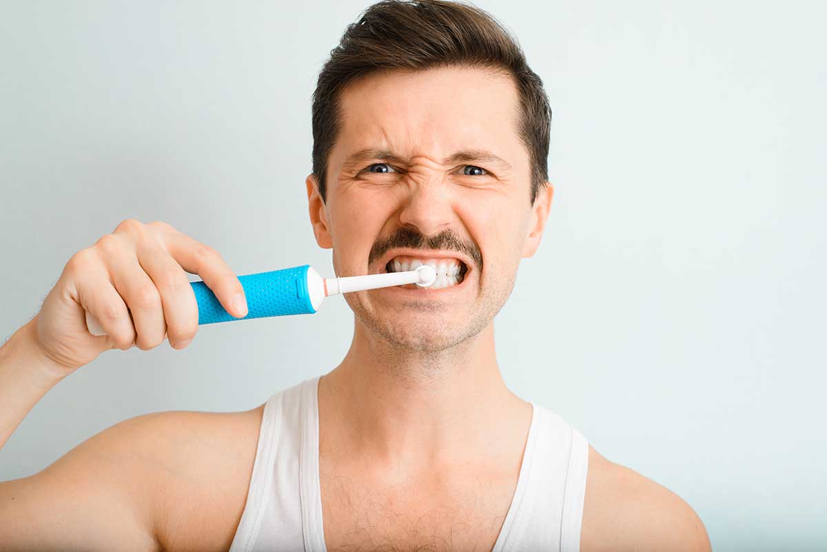 photo of a man brushing his teeth too hard to show one of the habits that can damage teeth