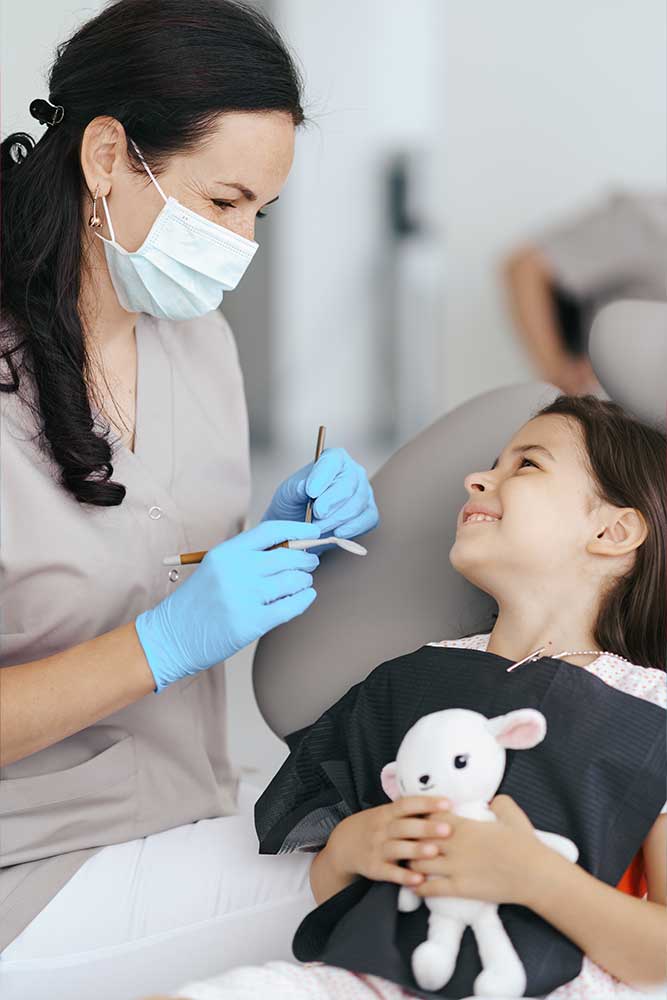 children's dentist speaking with a child who is holding a stuffed teddy bear