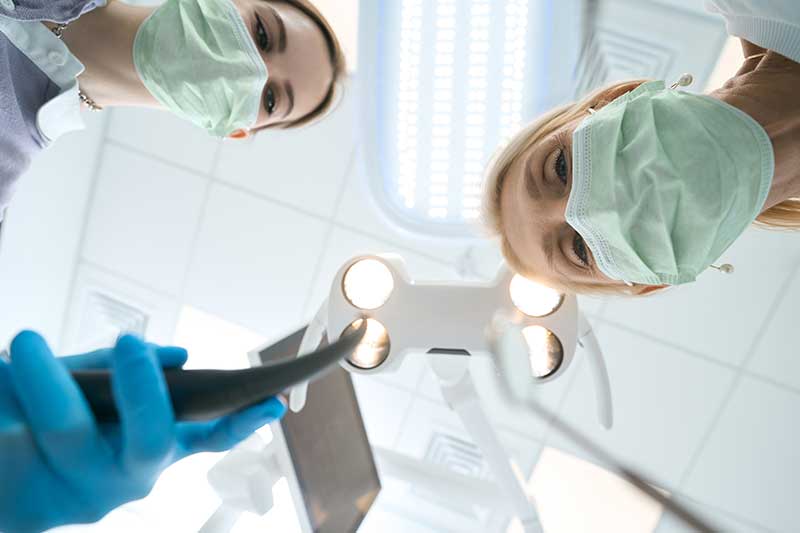 two oral surgeons lean in over a patient