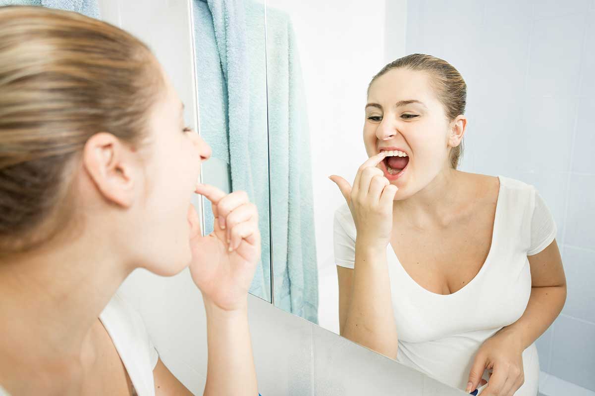 women scraping plaque off her teeth with a fingernail