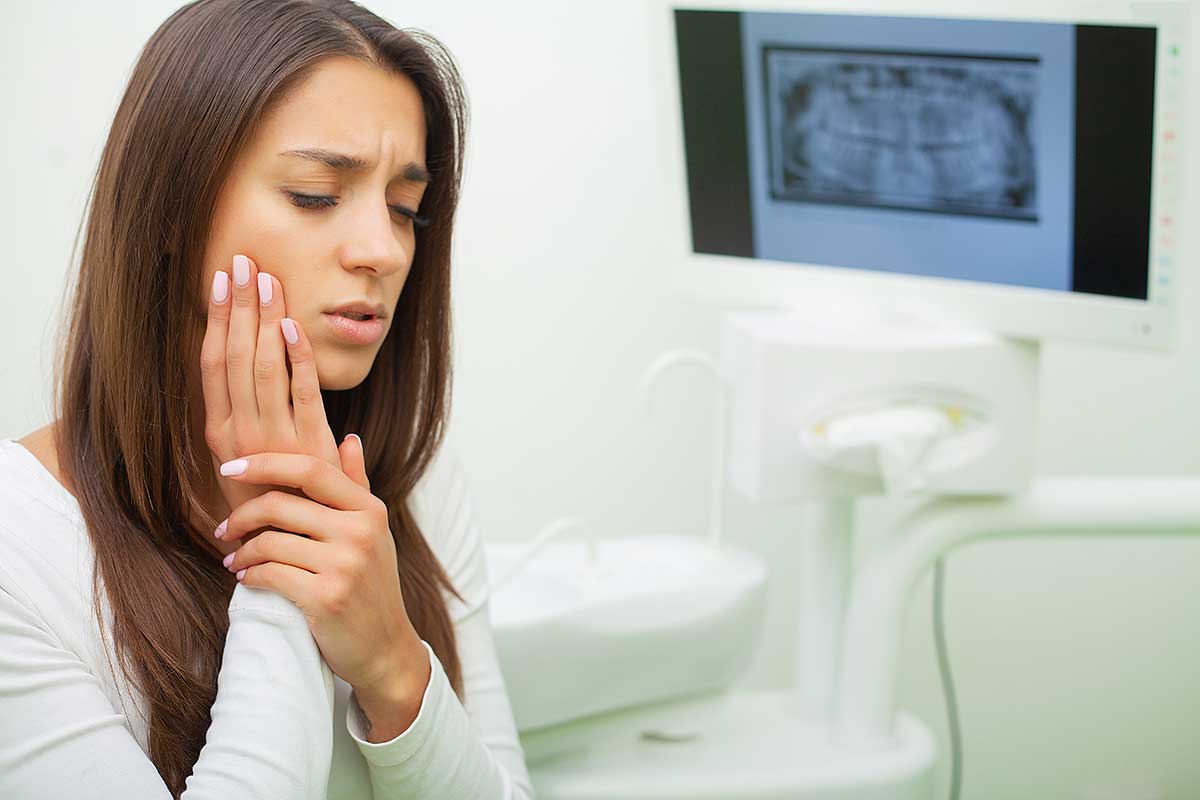 woman holds her hand to her cheek as she experiences a common dental health issue - a toothache