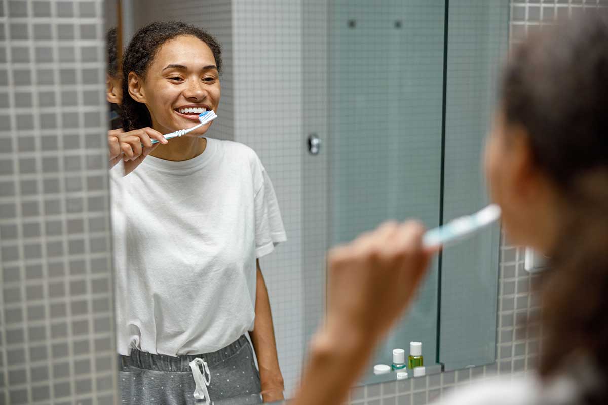 teenage girl brushing her teeth in the mirror smiling