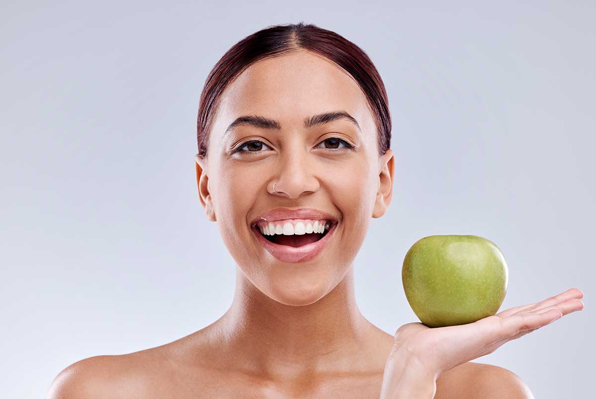 woman holding up an apple as part of her preventative dentistry healthy diet plan