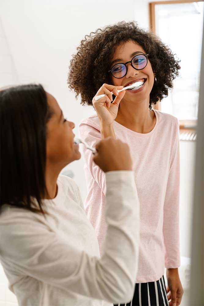 sisters brushing teeth together in the mirror and smiling at each other