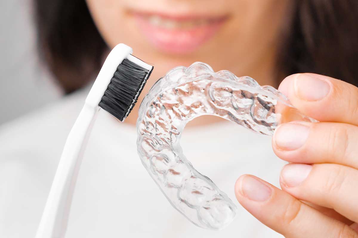 woman uses a toothbrush to clean her clear aligners
