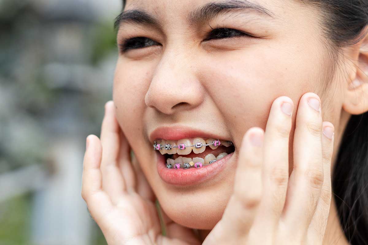 young girl holds her face because her braces are causing discomfort